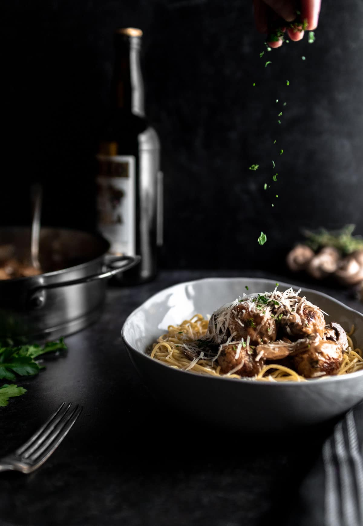 Hand sprinkling herbs on chicken meatballs with mushrooms and marsala cream sauce.