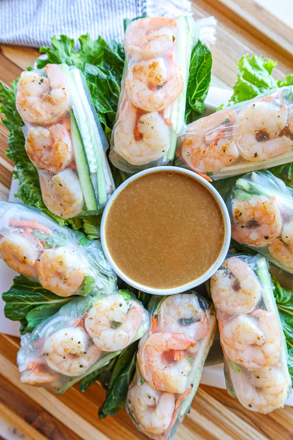 Vietnamese shrimp spring rolls with peanut sauce on a wooden cutting board.