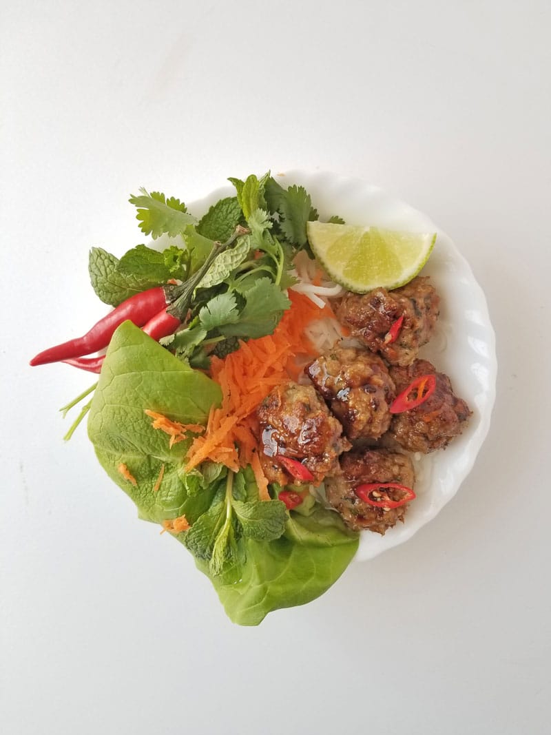 Sticky chicken Thai meatballs on a white plate with vegetables, lime, and chilies.