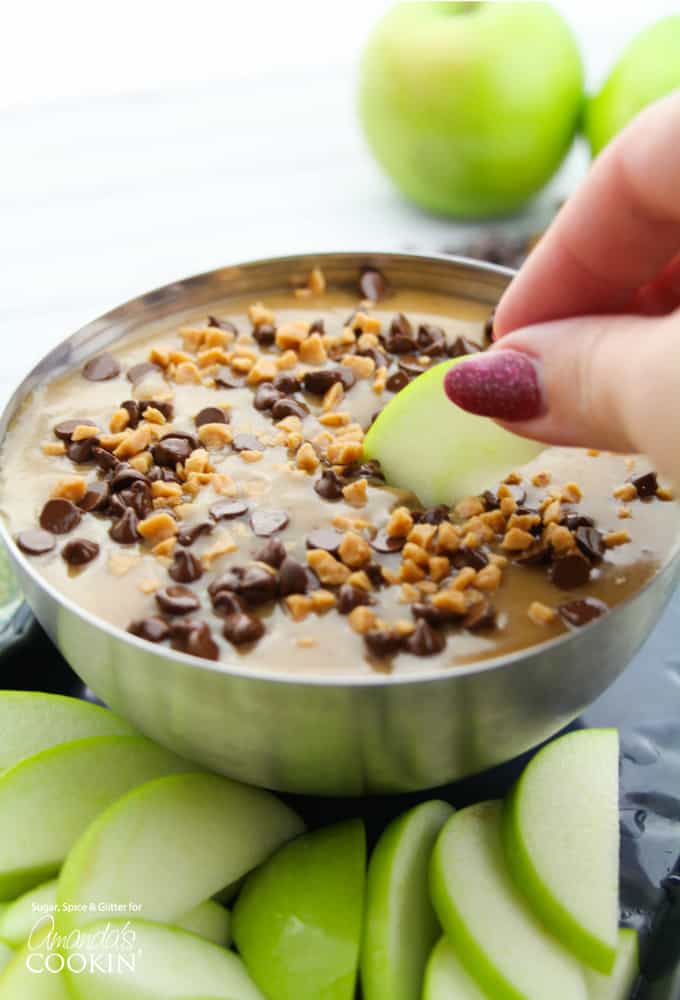 Hand dipping apple slice into caramel apple dip.