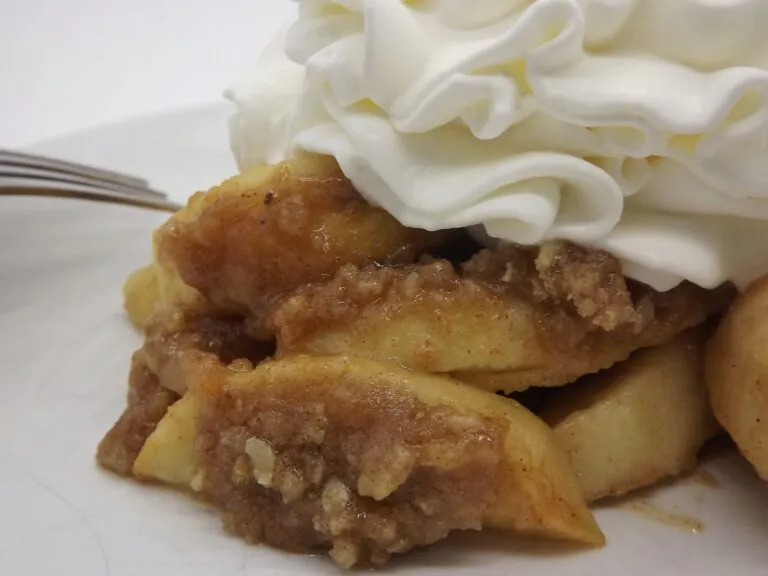 Smoked apple crisp with whipped cream on a white plate.