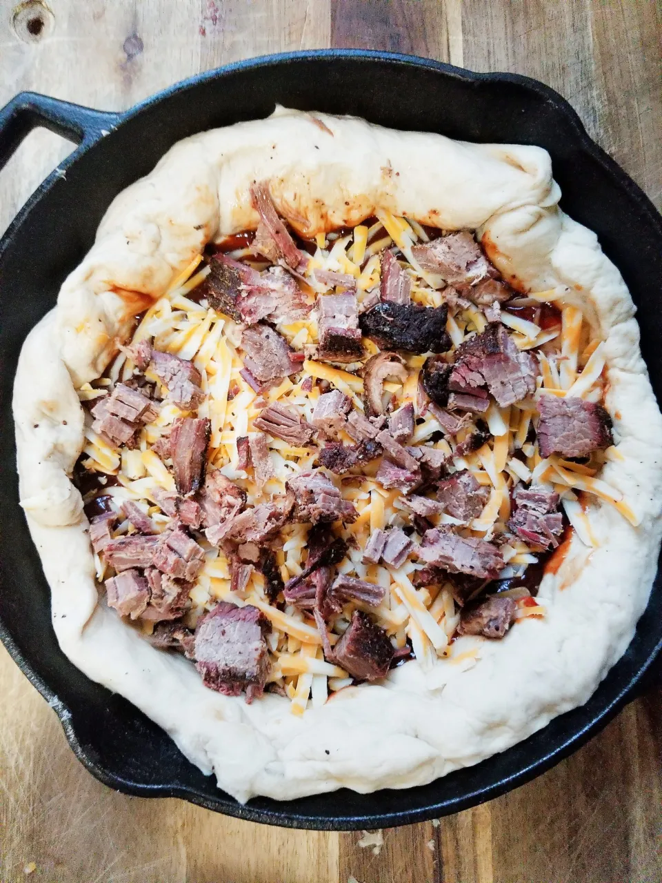 Uncooked leftover brisket bbq pizza in a cast iron pan.