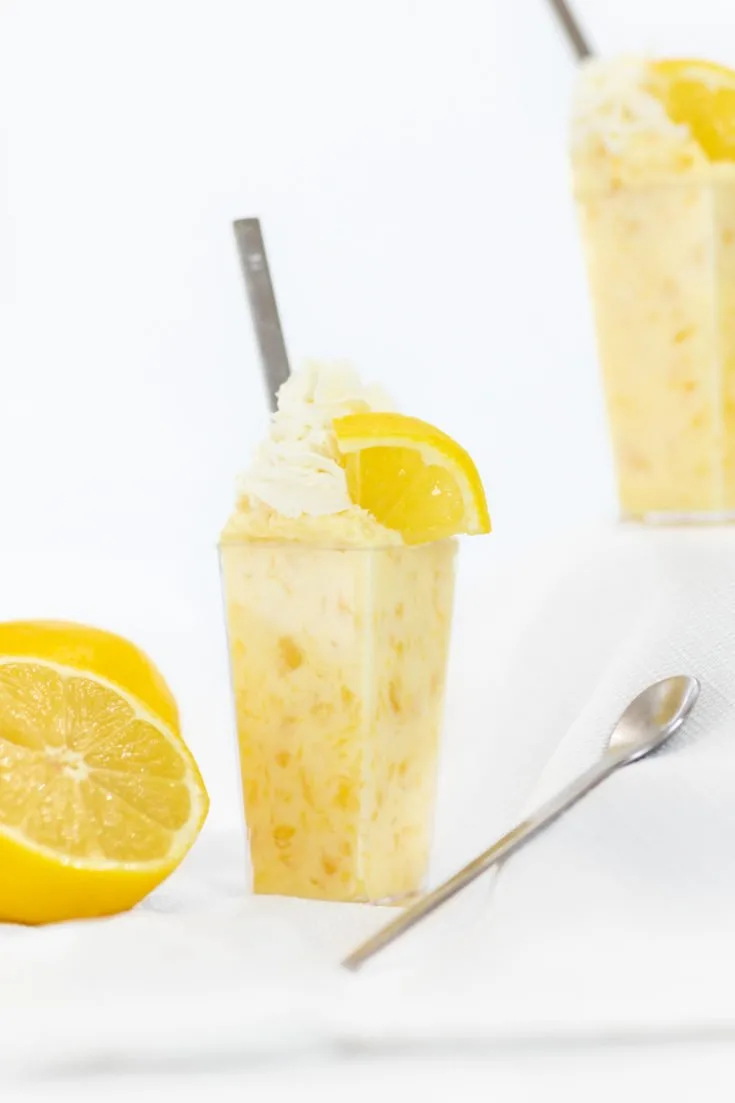 Pineapple lemon dessert in a fancy dessert cup with a skinny spoon and sliced lemons.