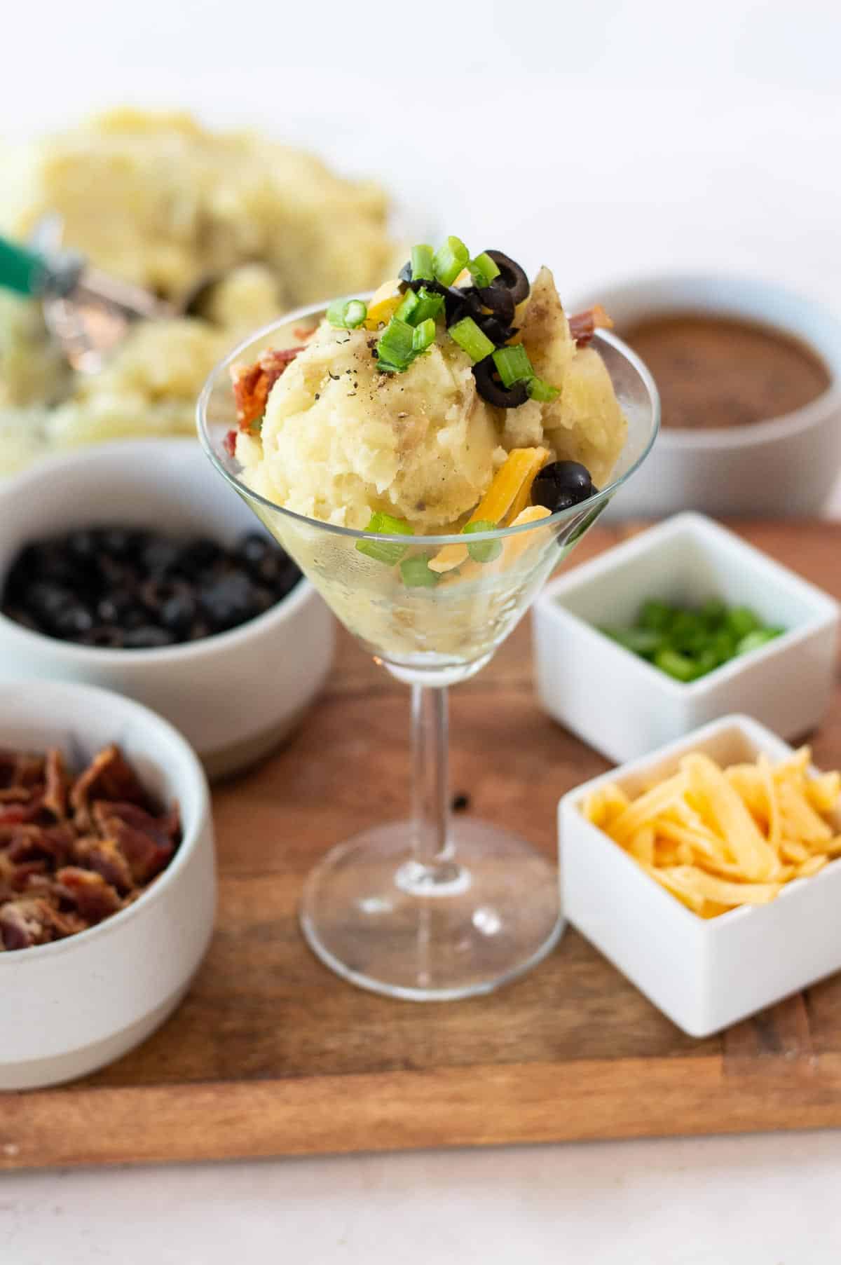 Loaded mashed potatoes in a martini glass with toppings in separate dishes.