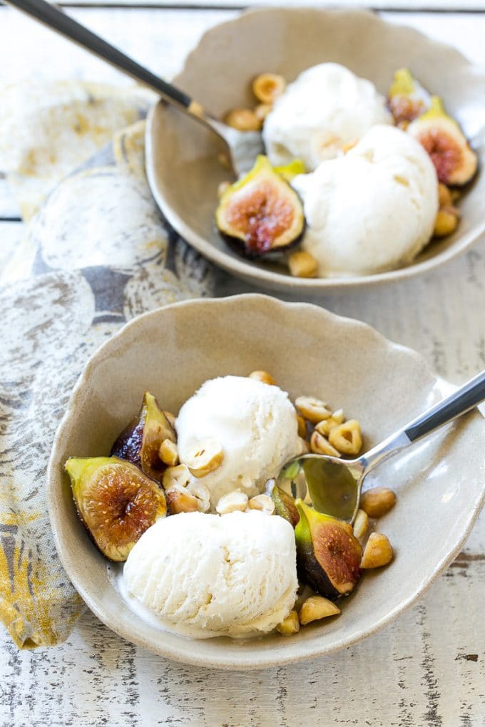 Spice roasted figs with ice cream and hazel nuts in a bowl with spoon.