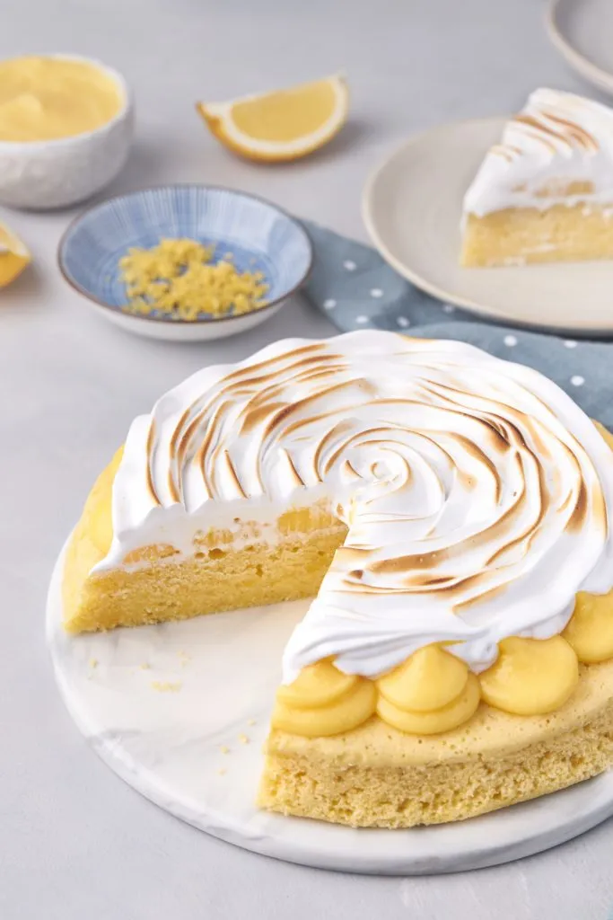 Lemon meringue cake with slice on a saucer in the background.