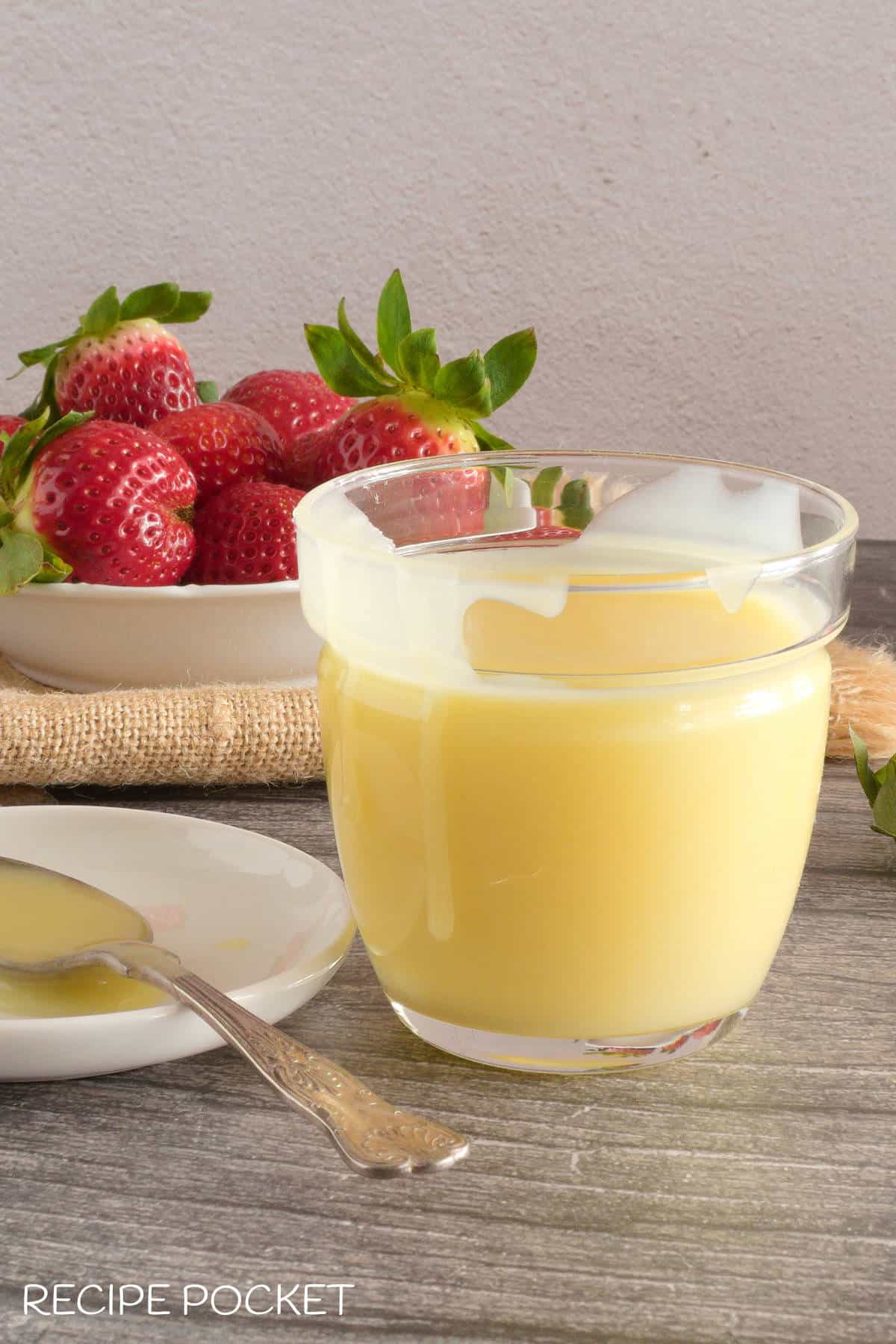 White chocolate sauce in a clear container with strawberries in a bowl.