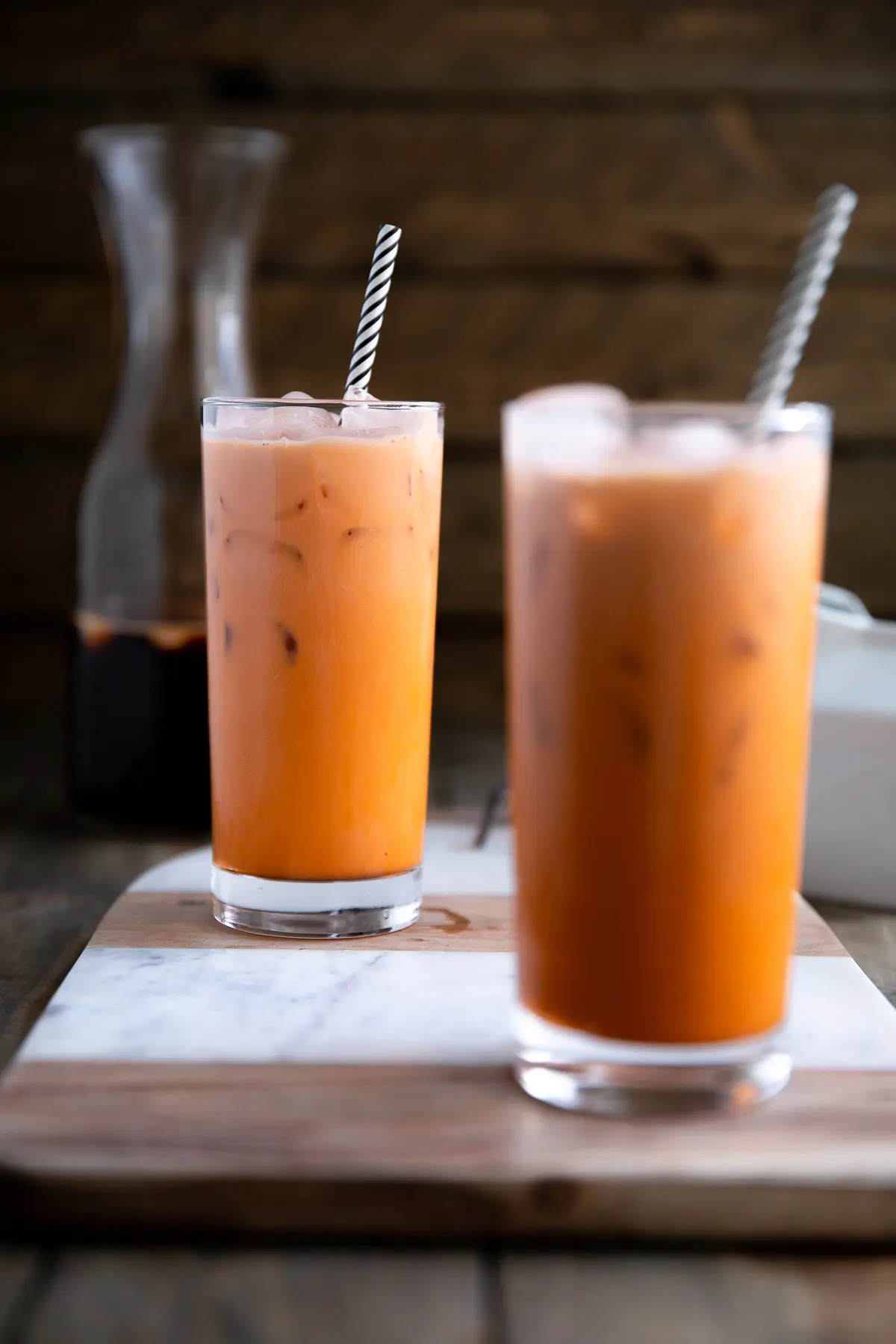 Thai iced tea served in a glass with black and white straw.