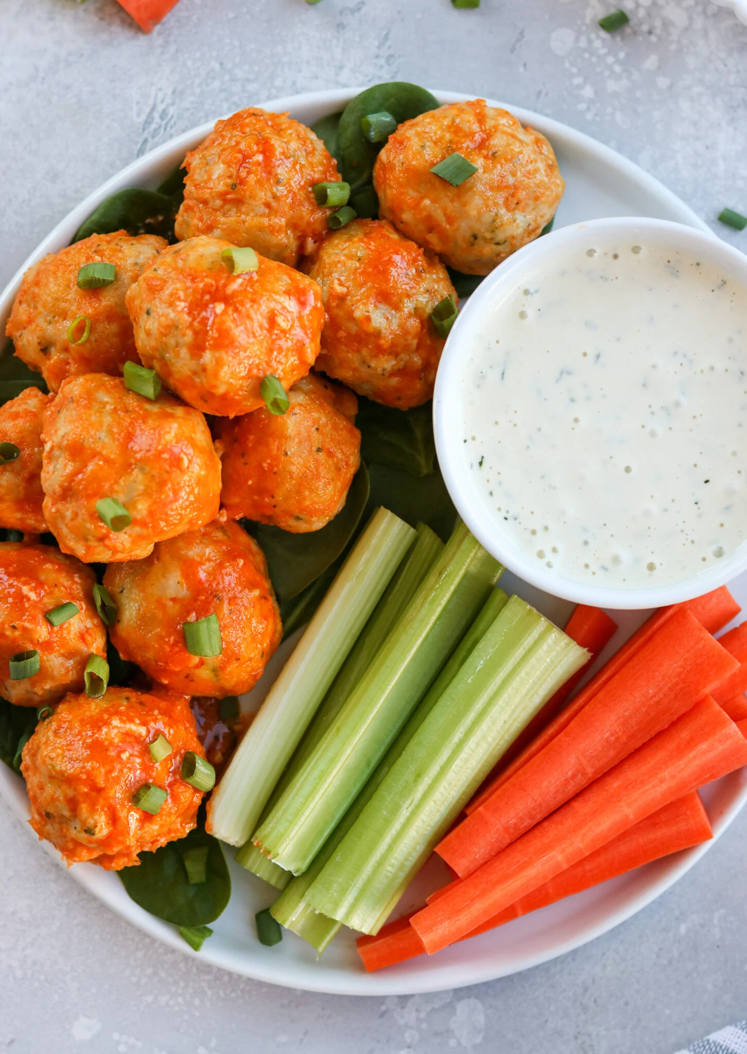 Buffalo chicken meatballs with celery and carrots and dipping sauce on a plate.