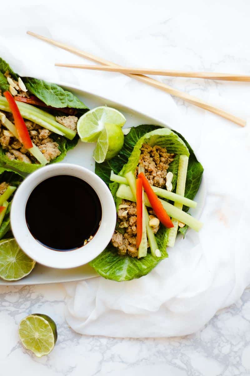 Thai lettuce wraps served on a white tray with lime in soy sauce with chopsticks close by.
