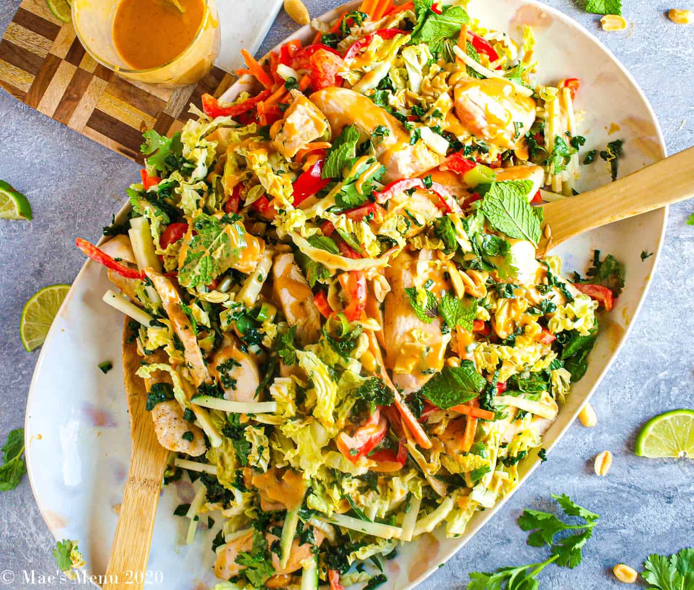 Thai chicken salad with peanut dressing on a serving platter with wooden serving spoons.