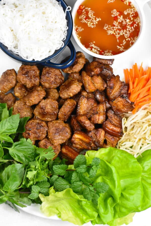 Bun cha recipe with greens, meatballs, bean sprouts, carrots, and broth on a white background. 