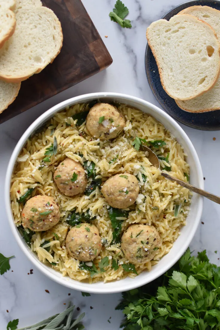 Easy chicken meatballs with orzo pasta in a white bowl with bread in the background.