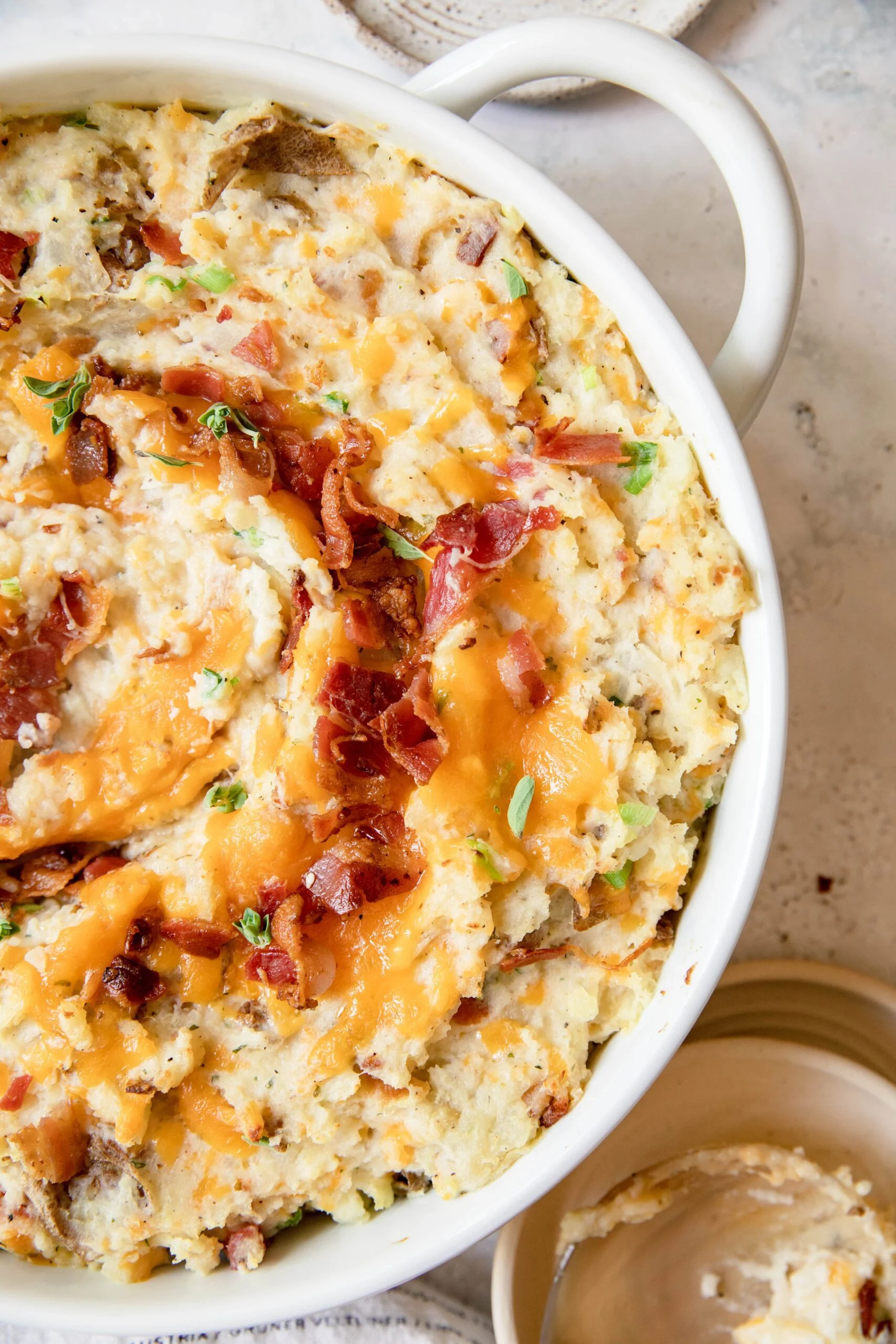 Loaded mashed potatoes with bacon, cheese, and herbs in a white baking dish.