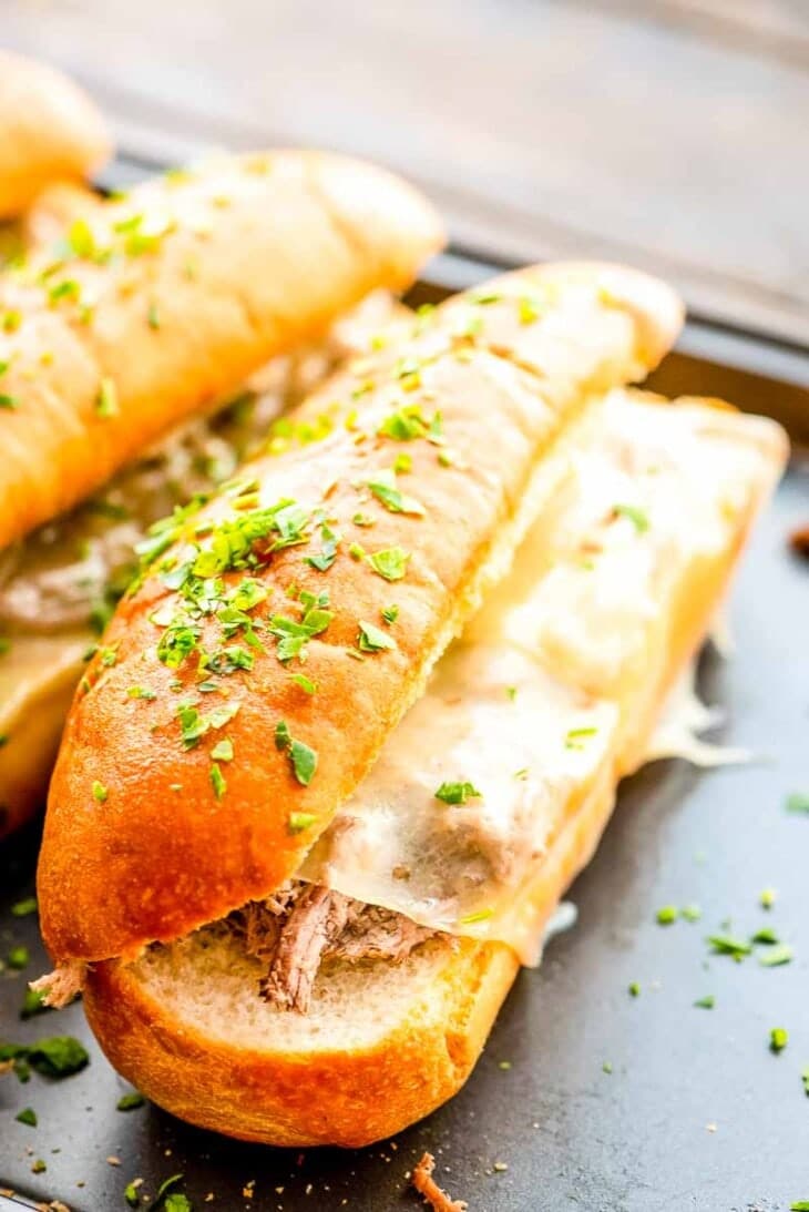 Shredded beef French dip sandwiches on a pan.