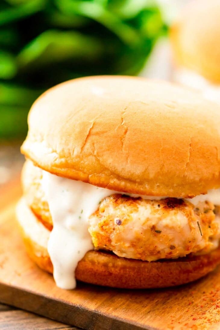 Ground chicken burger with ranch on a wooden cutting board.