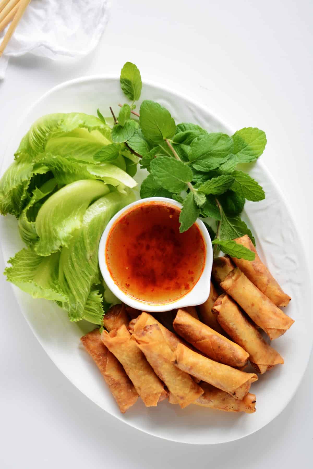 Vietnamese prawn spring rolls with lettuce and mint on a white tray.