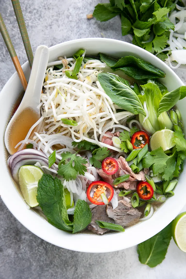 Pho soup with meat, bean sprouts, and limes in a white bowl.