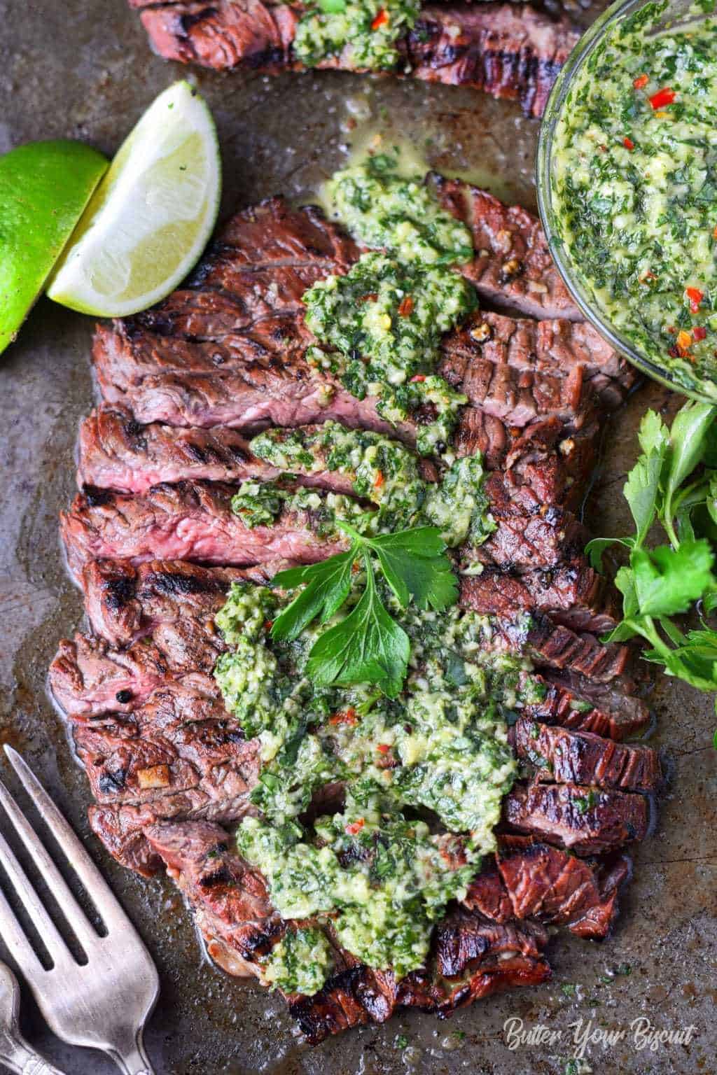 Grilled skirt steak with chimichurri with lime wedges and fork.