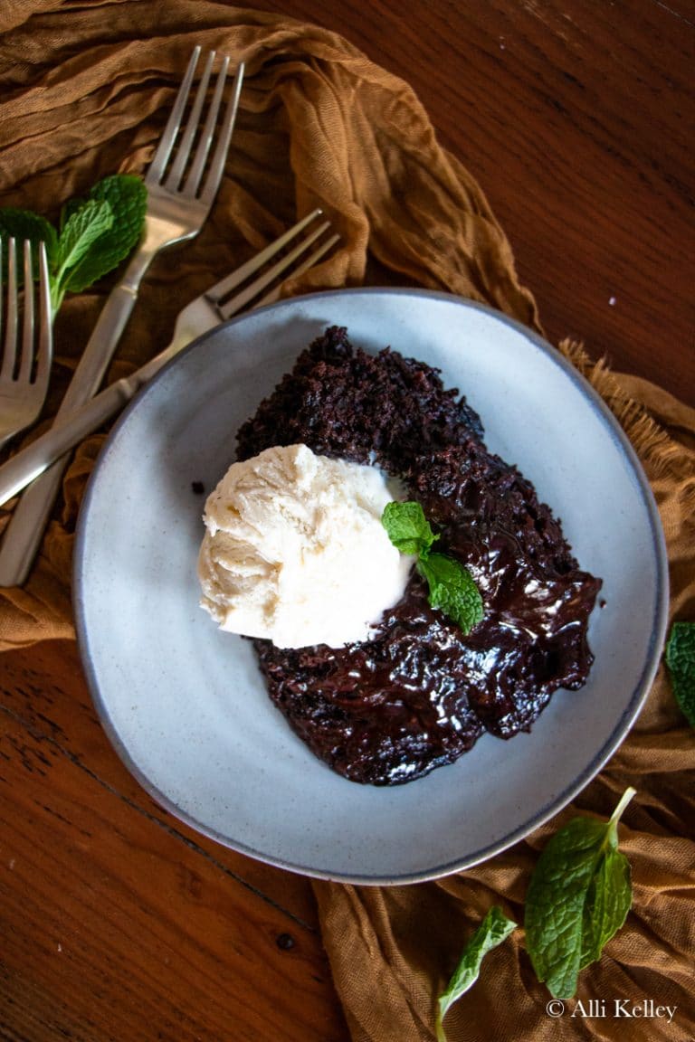 Crockpot chocolate lava cake with vanilla ice cream on a gray plate with forks in the background.