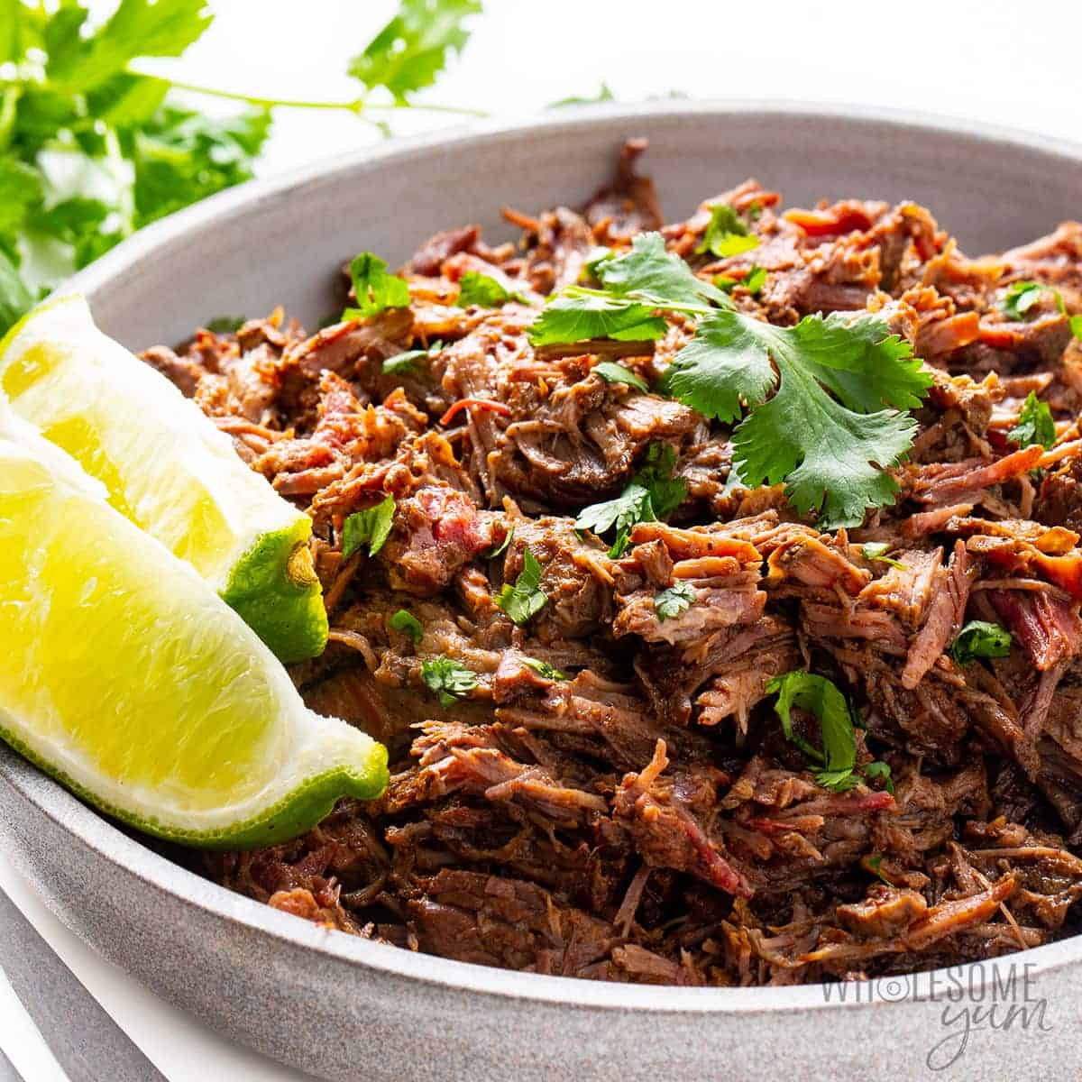 Chipotle beef barbacoa with lime wedges.