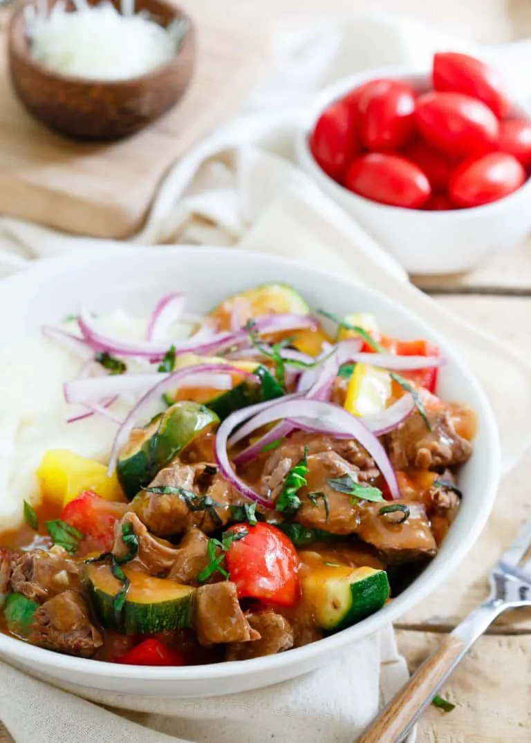 Slow cooker beef stew with zucchini, tomatoes, and onions in a bowl.