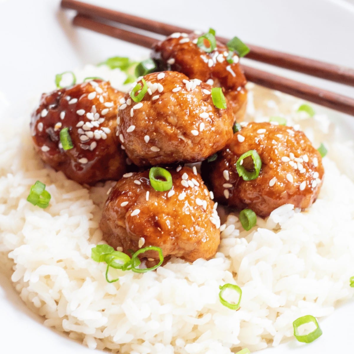 Sweet sesame ginger meatballs atop rice with chopsticks.