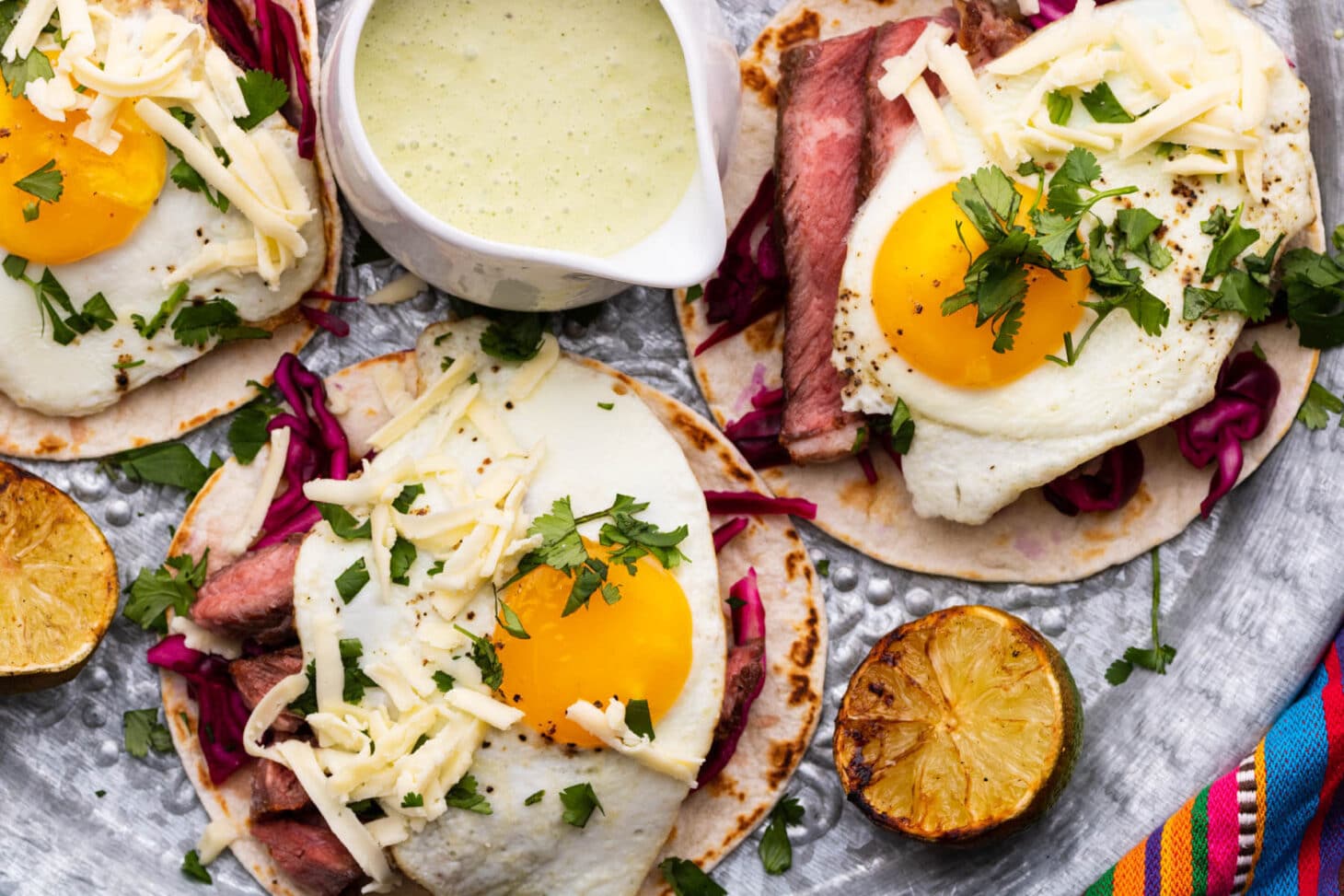 Grilled steak and egg tacos with sauce and limes.