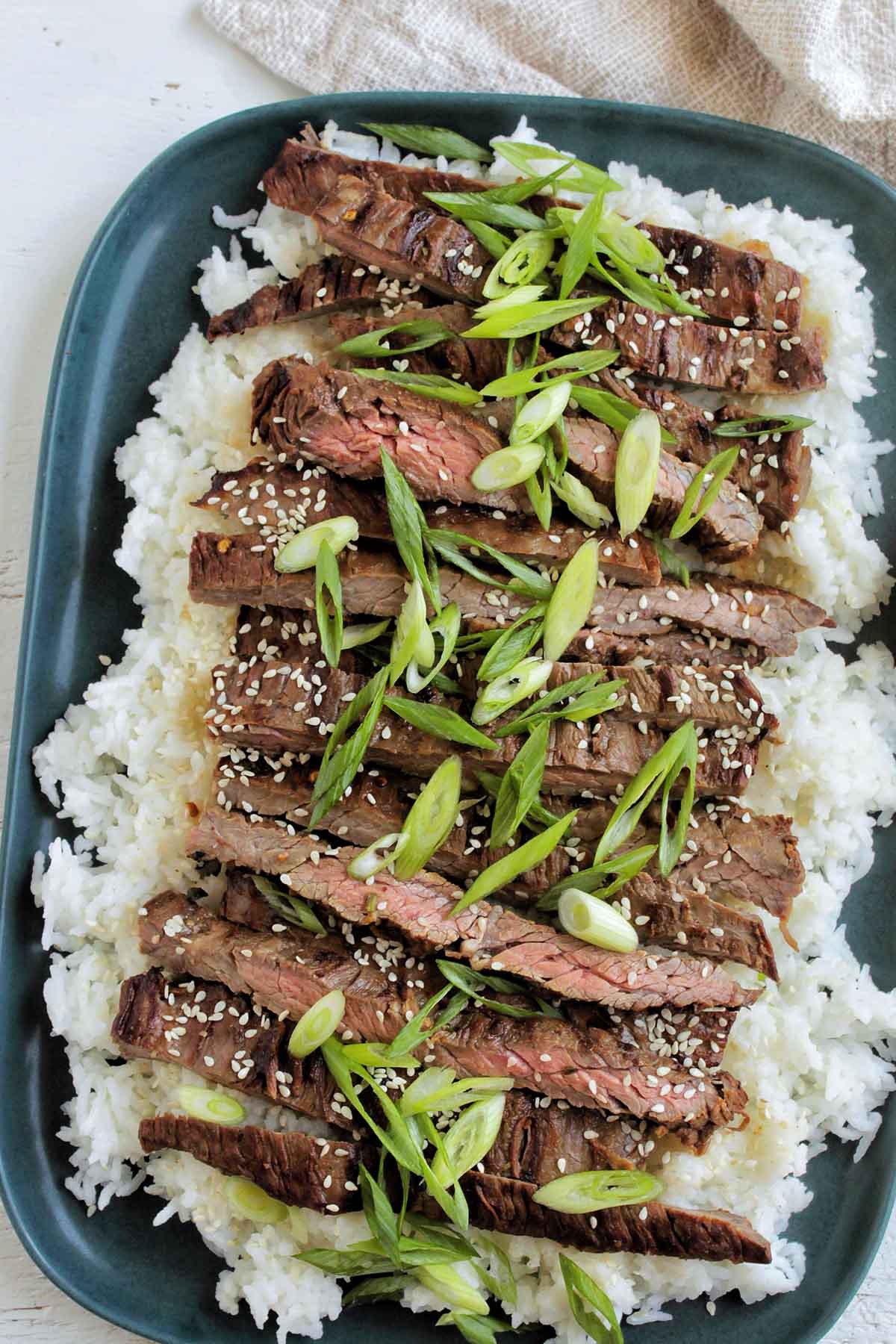 Grilled Asian marinated skirt steak with sliced green onions on top of white rice.