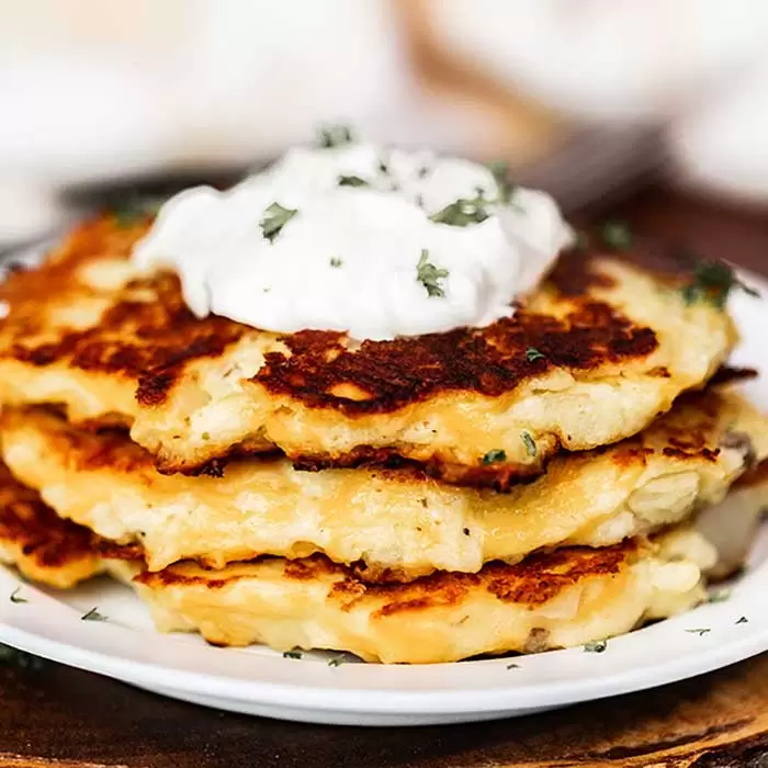 Stack of mashed potato cakes with sour cream.