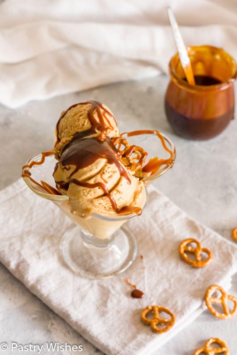 Salted caramel pretzel ice cream with caramel sauce in a decorative clear container.