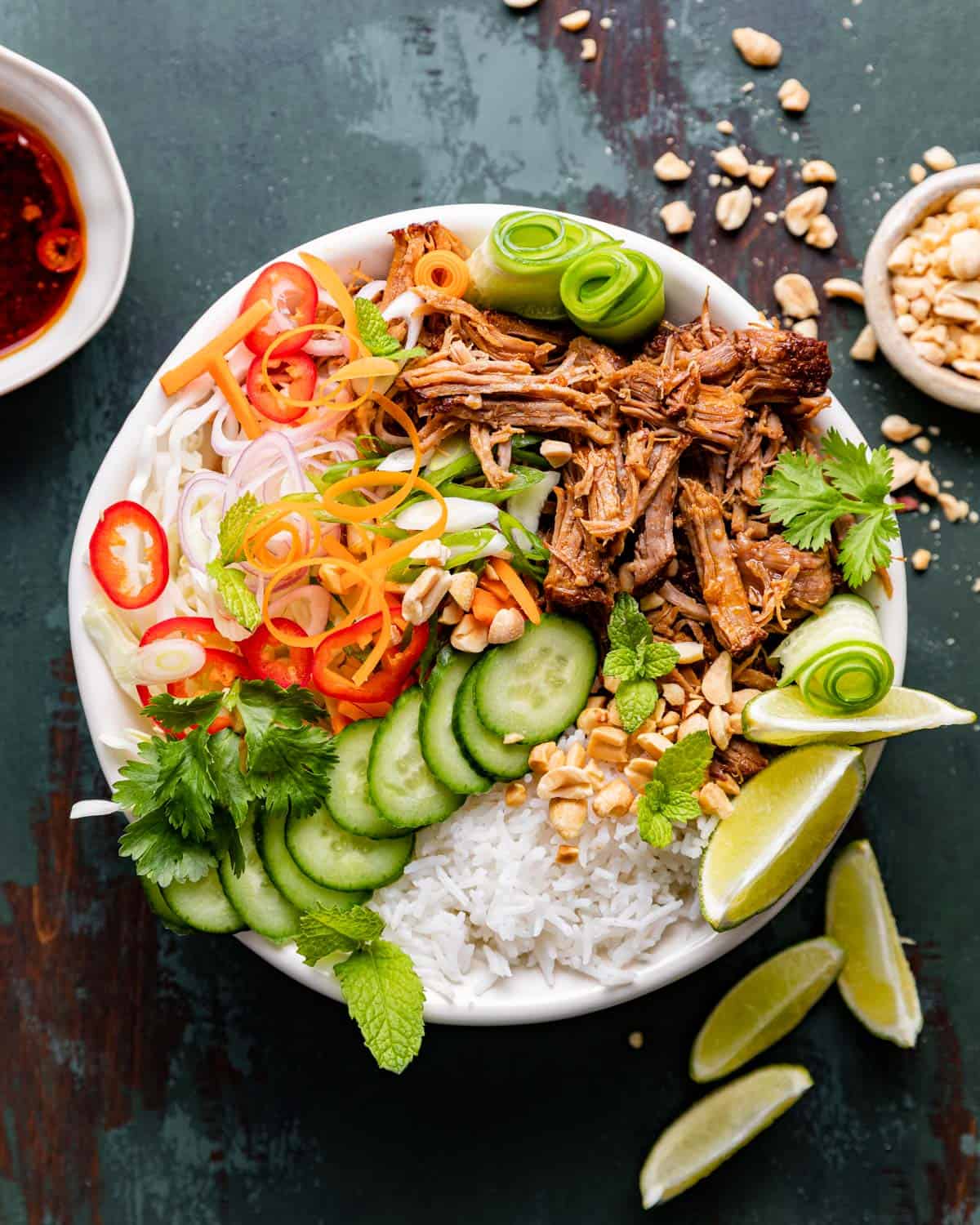 Bowl of Asian pulled pork bowl with cucumber, lime, cucumber, peanuts, and rice.