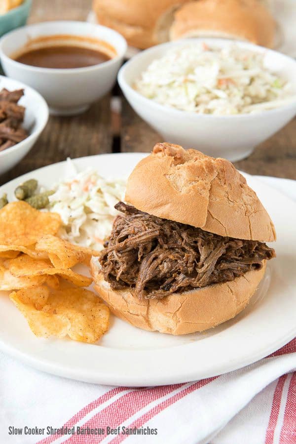 Slow cooker shredded barbecue beef sandwich on a plate with coleslaw and chips.