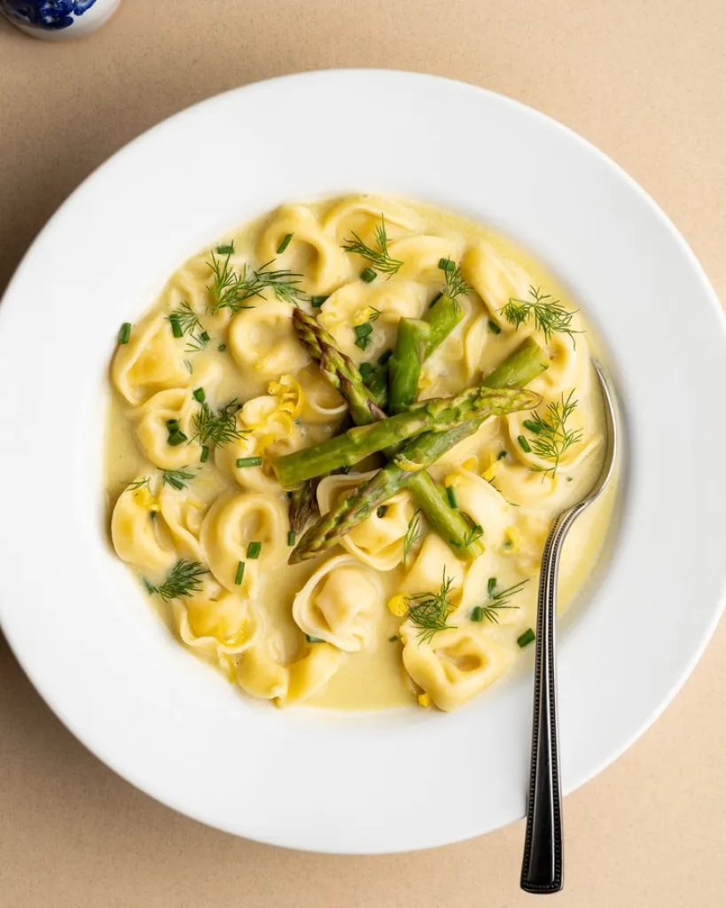 Overhead shot of tortellini in asparagus broth in a white bowl.