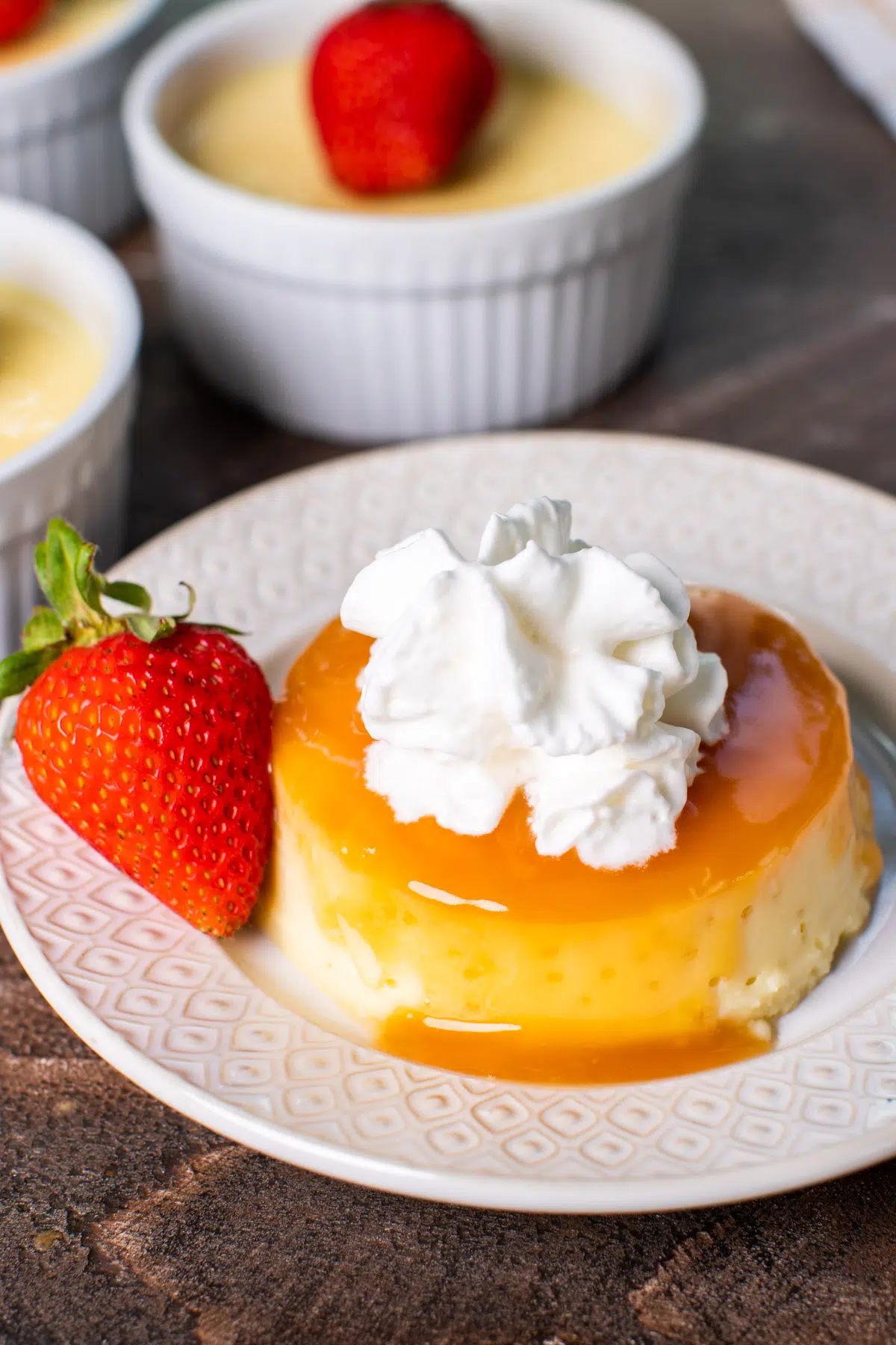 Flan with whipped cream and a strawberry on decorative white plate.