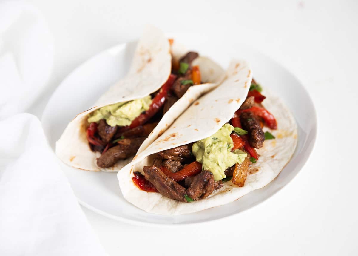 Steak fajitas in flour tortillas on a white plate.