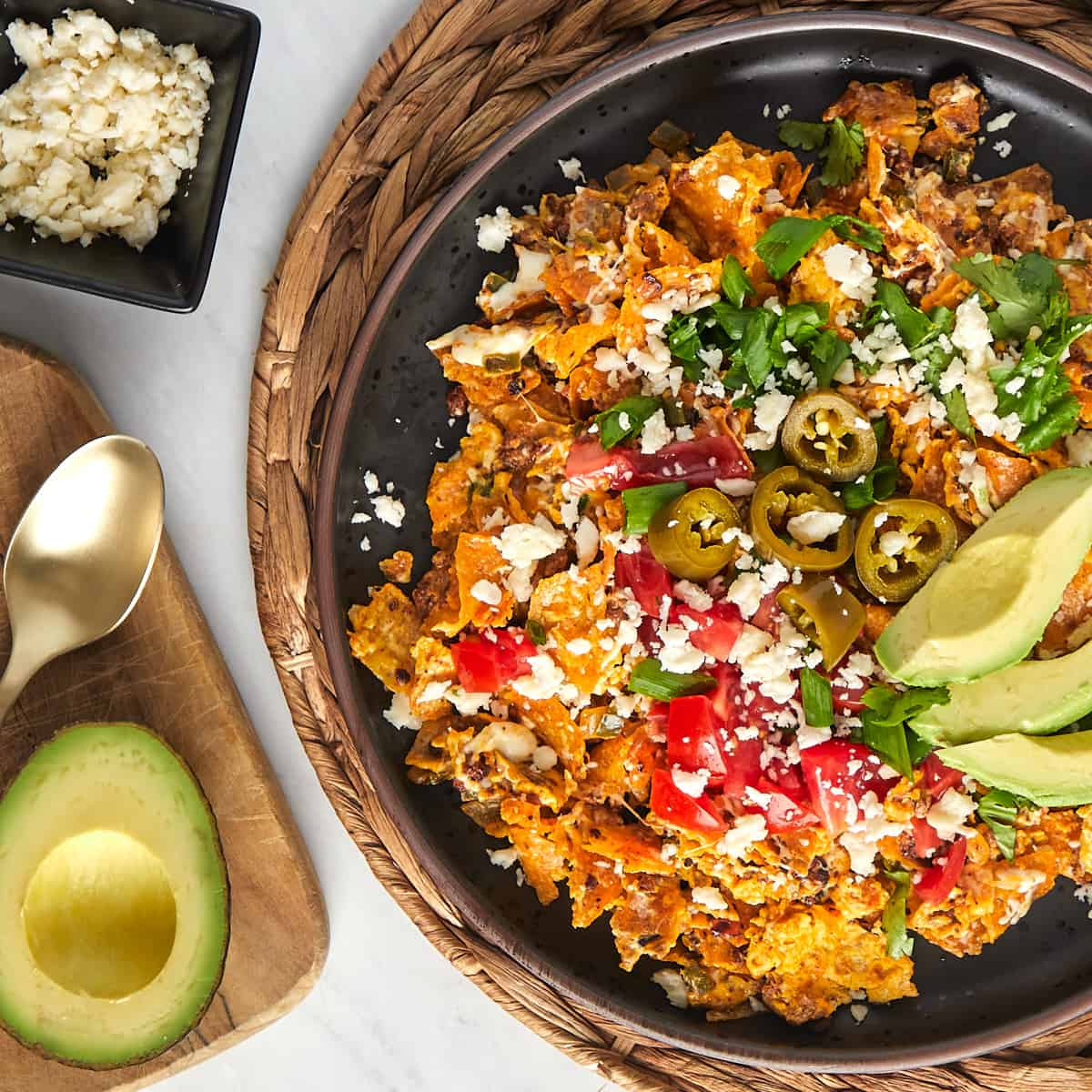 Tex Mex migas with chips tomatoes, jalapenos, cotija, and avocado slices on a plate.