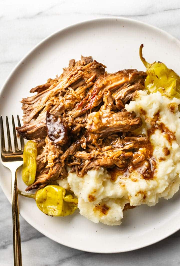 Mississippi pot roast with peppers over mashed potatoes on a white plate.