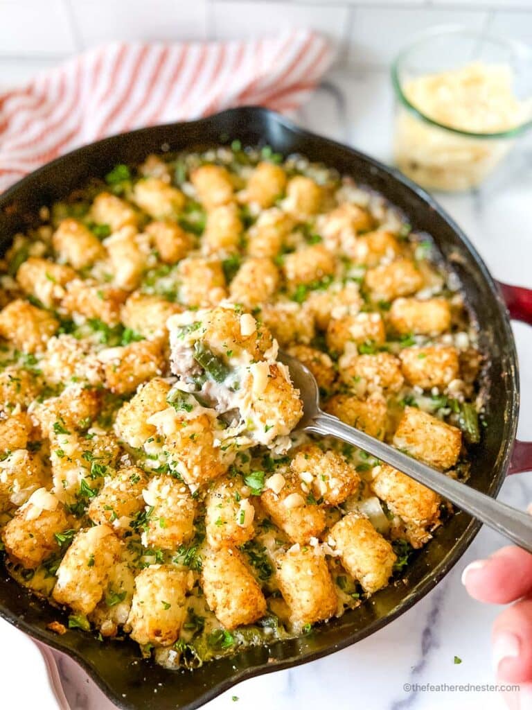 Spoon scooping tater tot turkey casserole in a cast iron skillet.