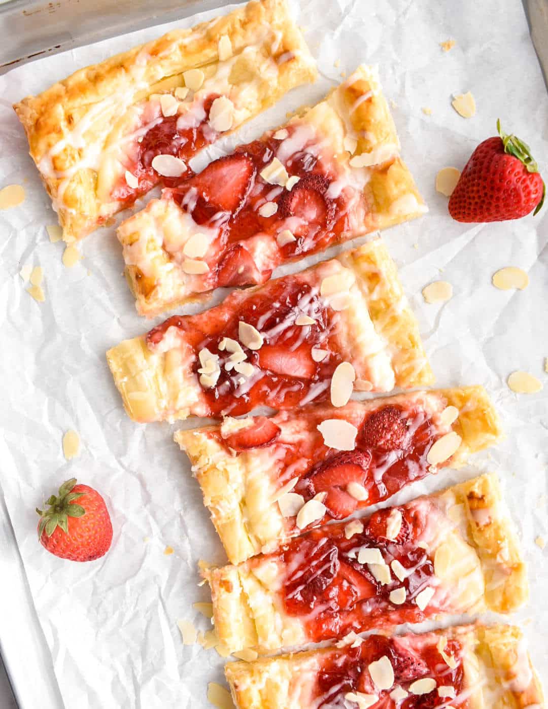 Strawberry cream cheese Danish cut into pieces on crinkled parchment paper.