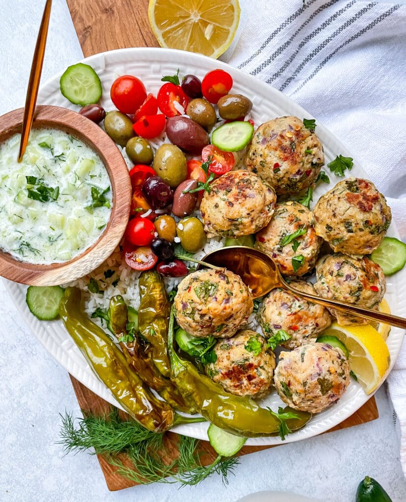 Colorful Greek chicken meatballs on a plate with vegetables and tzatziki sauce.