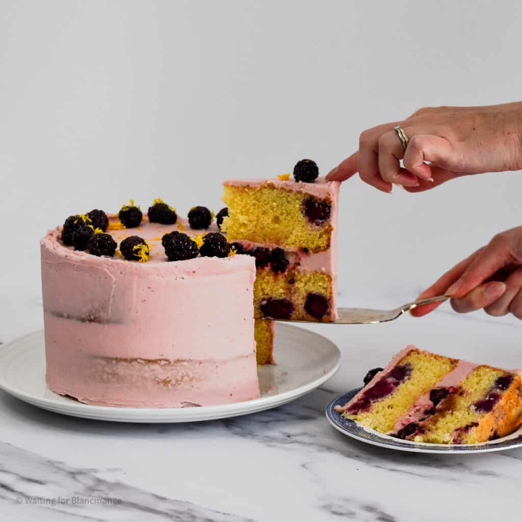 Hands picking up a slice of lemon blackberry cake.