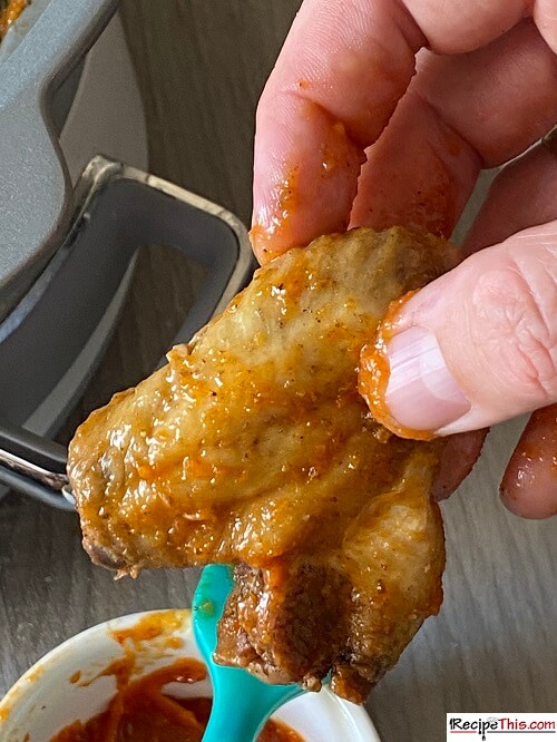 Hand holding a chicken wing doused in sauce.