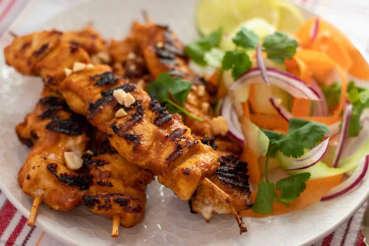 Chicken satay skewers on a plate with vegetables.