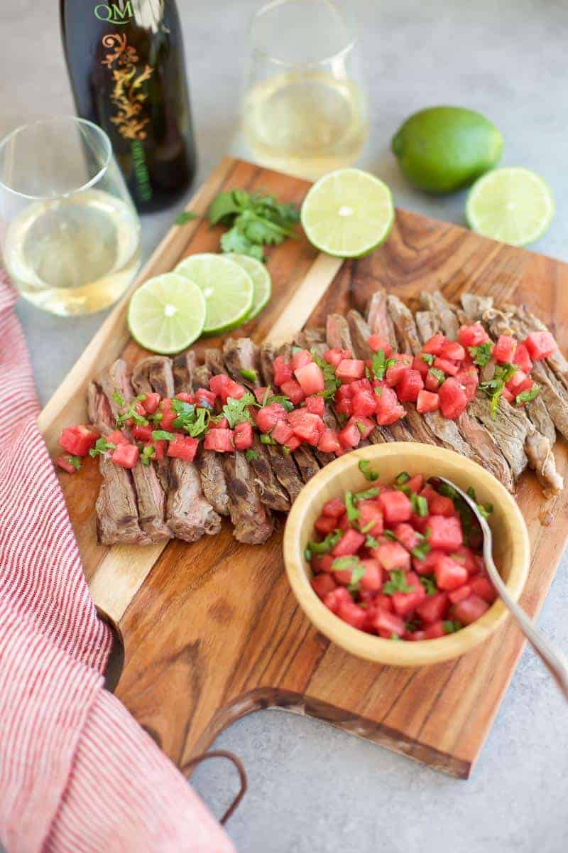 Grilled skirt steak with watermelon salsa on a wooden cutting board with sliced lime.