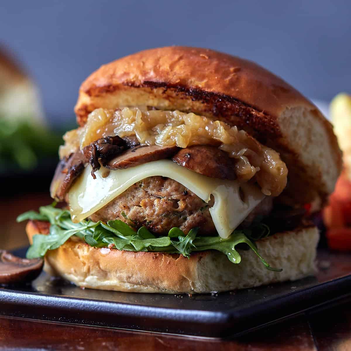 Caramelized onion mushroom Swiss turkey burger on black rectangular plate.