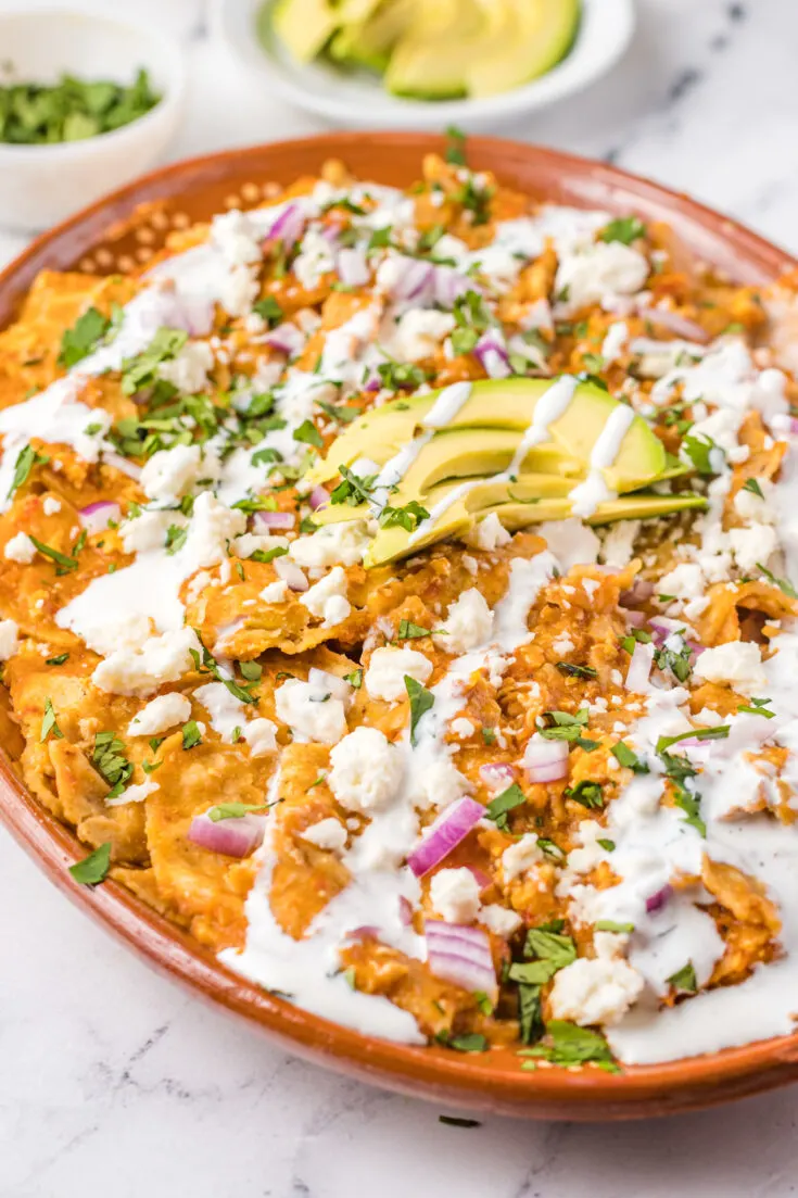 Chilaquiles rojos recipe with avocado, sauce, and cheese on a plate.