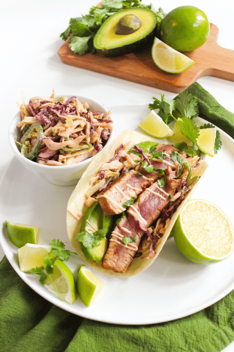 Seared ahi tuna fish taco on plate with ingredients in the background.