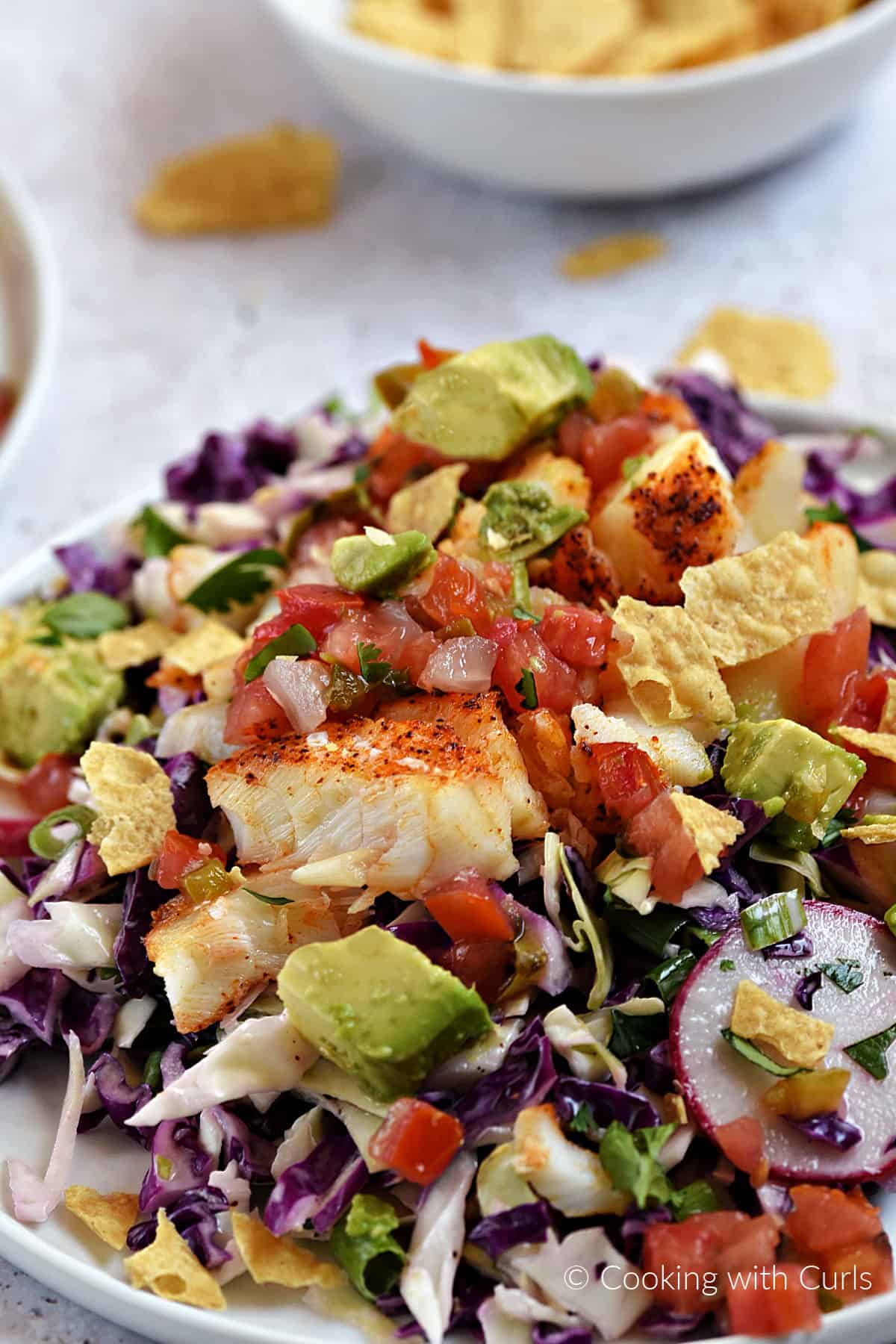 Fish taco salad with avocado, cabbage, salsa, and crushed chips on s plate.