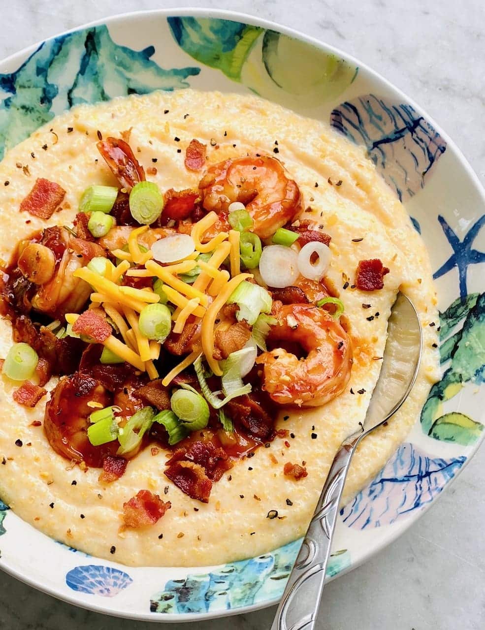 Southern shrimp and grits with scallions and cheese in a decorative bowl.